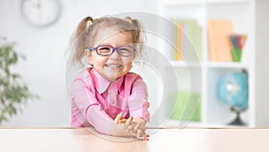 Happy kid girl in eyeglasses sitting at table photo