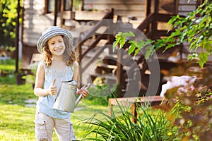 happy kid girl in hat playing little gardener and helps to water flowers