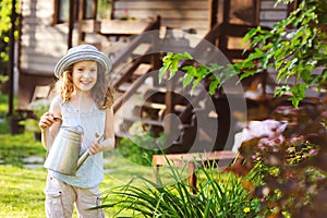 happy kid girl in hat playing little gardener and helps to water flowers