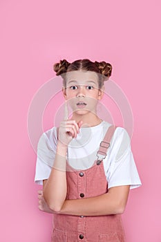 Happy kid girl having idea, raising finger on pink background