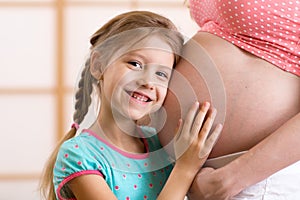 Happy kid girl hugging pregnant mother's belly