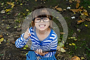 Happy kid girl looking in camera with happy and peaceful expression in glasses, holding in his hands pc tablet.