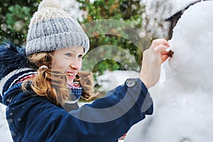 Happy kid girl making snow man on Christmas vacations on backyard