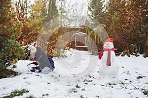 Happy kid girl making snow man on Christmas vacations on backyard