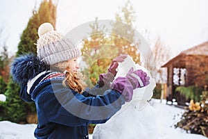 Happy kid girl making snow man on Christmas vacations on backyard