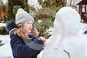 Happy kid girl making snow man on Christmas vacations on backyard