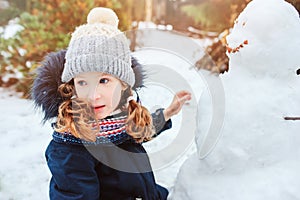 Happy kid girl making snow man on Christmas vacations on backyard