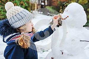 Happy kid girl making snow man on Christmas vacations on backyard