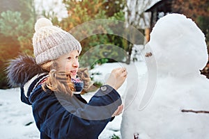 Happy kid girl making snow man on Christmas vacations on backyard