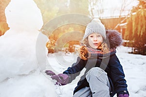 Happy kid girl making snow man on Christmas vacations on backyard