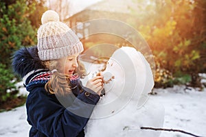 Happy kid girl making snow man on Christmas vacations on backyard