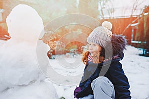 Happy kid girl making snow man on Christmas vacations on backyard