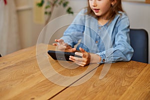 Happy kid girl playing game on mobile phone at home