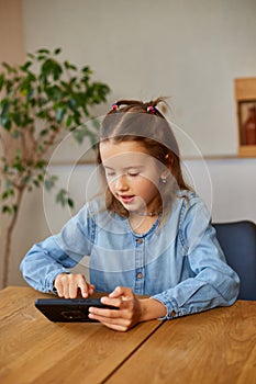 Happy kid girl playing game on mobile phone at home