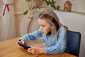 Happy kid girl playing game on mobile phone at home