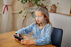 Happy kid girl playing game on mobile phone at home