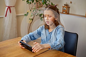 Happy kid girl playing game on mobile phone at home