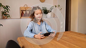 Happy kid girl playing game on mobile phone at home, child using smartphone