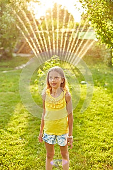 Happy kid girl playing with garden sprinkler run and jump, summer