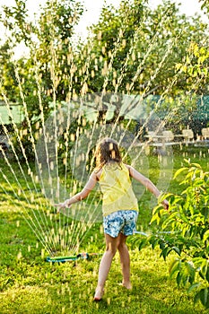 Happy kid girl playing with garden sprinkler run and jump, summer