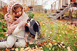 Happy kid girl playing with her cavalier king charles spaniel dog in autumn