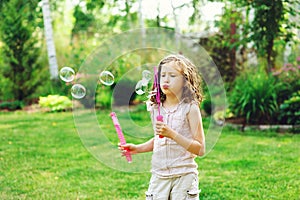 Happy kid girl playing with soap bubbles in summer