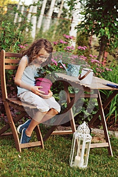 happy kid girl playing in summer garden, holding geranium flower in pot