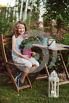 Happy kid girl playing in summer garden, holding heranium flower in pot