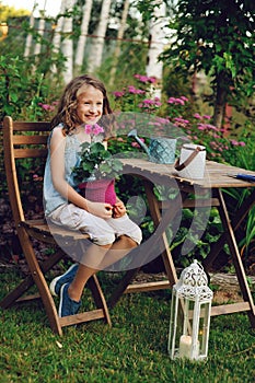 happy kid girl playing in summer garden, holding heranium flower in pot