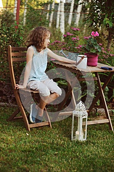 happy kid girl playing in summer garden, holding heranium flower in pot