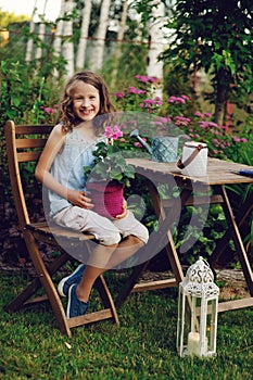 Happy kid girl playing in summer garden, holding heranium flower in pot