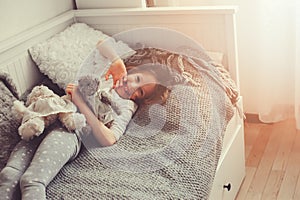 Happy kid girl playing with teddy bears in her room, sitting on bed