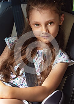 Happy kid girl sitting in the car in child seat with safety belt and smiling on summer green background. Closeup