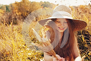 Happy kid girl in straw having fun outdoor on summer sunny field