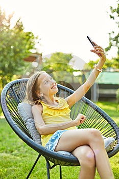 Happy kid girl take selfie on mobile phone in the park outdoor