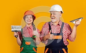 happy kid and grandfather plasterer in helmet on yellow background