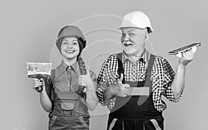 happy kid and grandfather plasterer in helmet on yellow background