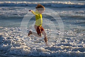 Happy kid have fun on tropical sea beach resort. Funny baby boy run with splashes by water pool along surf edge. Active