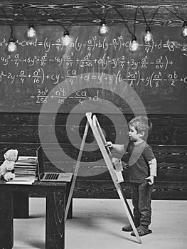 Happy kid having fun. Little boy writing on chalkboard. Side view kid in front of green board with math equation. Smart