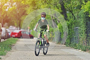 Happy kid having fun near home with a bicycle on beautiful spring day wearing protection mask for coronavirus Covid-19 pandemic