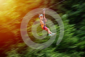 Happy kid with helmet and harness on zip line between trees. Panning effect