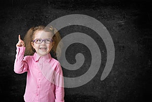 Happy kid inventor with rised hand thinking and finding idea near school black chalkboard