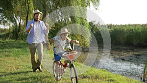 Happy kid learning to ride bike with the help of his parent at rural on background outdoor nature