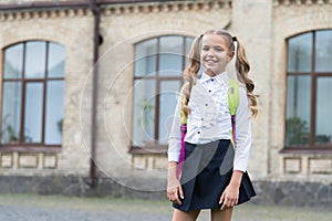 Happy kid with long hair tails back to school wearing fashion uniform in schoolyard outdoors, September 1