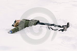 Happy kid making snow angel. Boy playing on a winter walk in nature. Child enjoying snowy weather