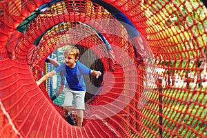 Happy kid overcomes obstacles in rope adventure park. Summer holidays concept. Little boy playing at rope adventure park. Modern photo
