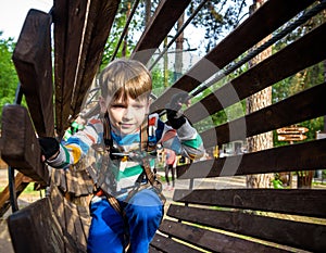 Happy kid overcomes obstacles in rope adventure park. Summer holidays concept. Little boy playing at rope adventure park. Modern