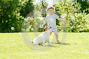 Happy kid and pet dog playing with soap bubbles at backyard lawn