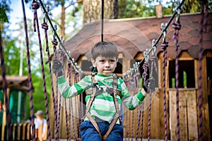 Happy kid playing at adventure park, holding ropes and climbing wooden stairs