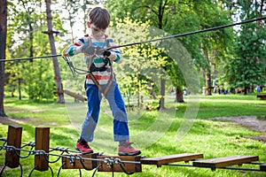 Happy kid playing at adventure park, holding ropes and climbing wooden stairs